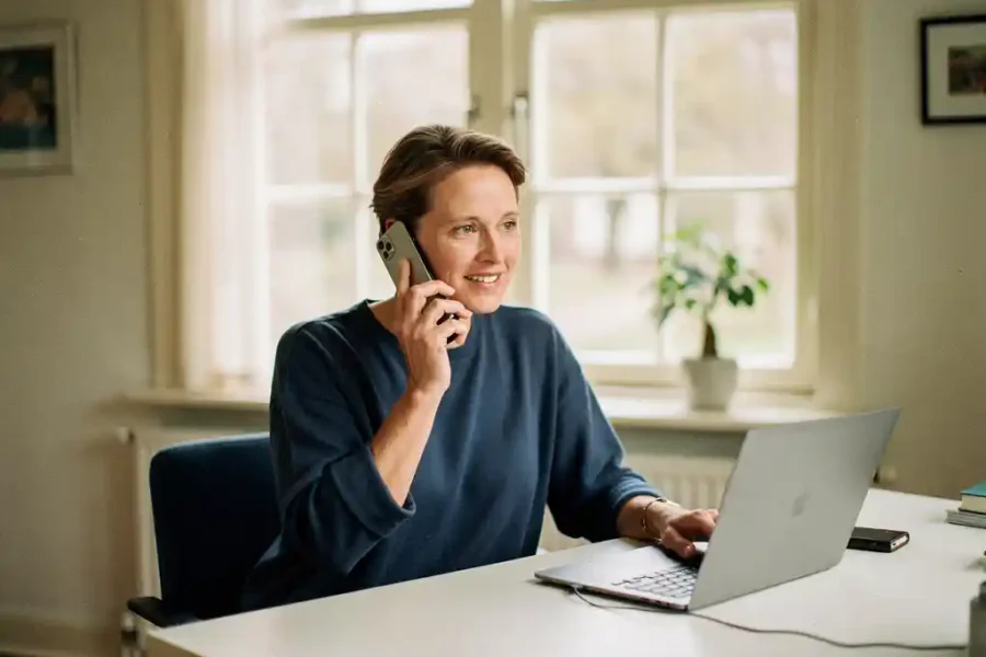 Professional aan bureau in lichte Nederlandse thuiswerkplek, belt via draadloze telefoon met laptop open, zacht daglicht door grote ramen.